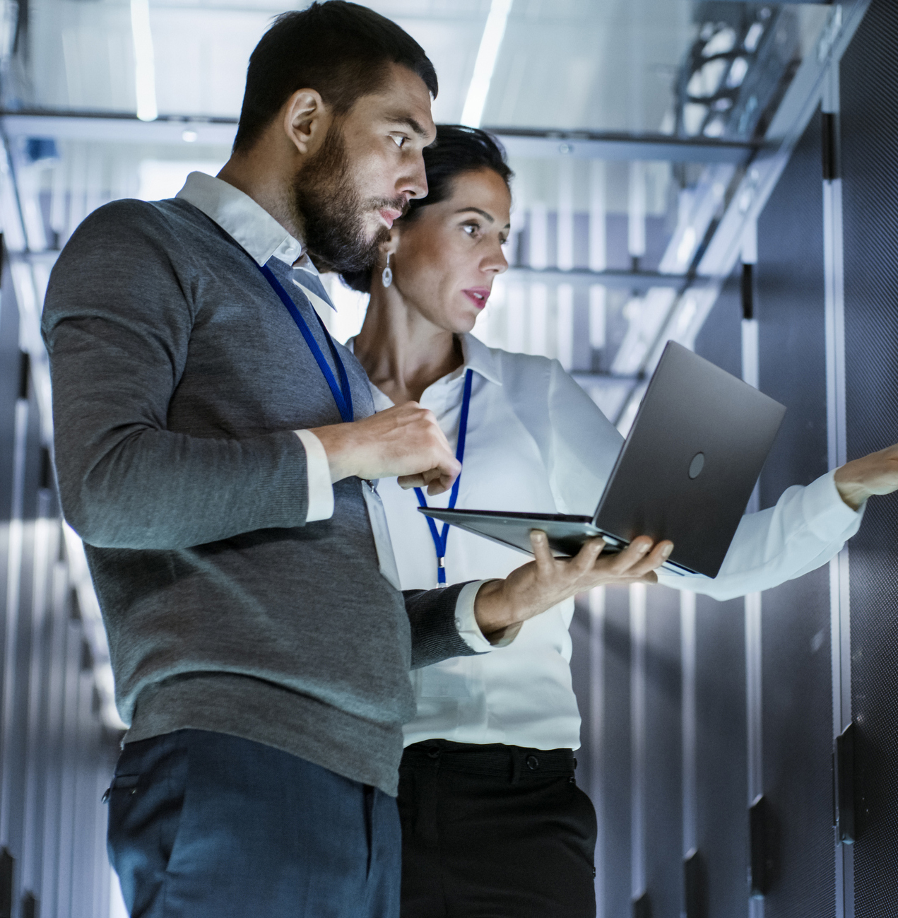Male IT Specialist Holds Laptop and Discusses Work with Female Server Technician. They're Standing in Data Center, Rack Server Cabinet is Open.